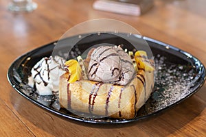 Honey toast with Chocolate and Vanilla ice-cream and whipped cream on a black plate.