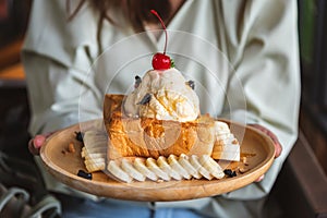 Honey toast, french toast with vanilla ice cream and honey on buttered bread in wooden plate holding by woman hand