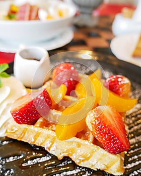 Honey waffle with strawberry and peach and icing sprinkle on black plate