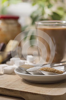 Honey, white sugar, cane sugar in the foreground enlarged. In the background, sugar cubes lie on a wooden board.