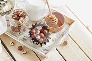 Honey in the wooden bowl, hazelnuts and jar with milk on the wooden tray