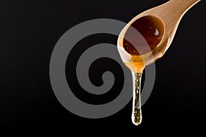 Honey in Wooden Spoon dripping isolated on black background