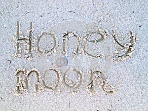 Honeymoon writing at the sand. Beach with wedding rings and honey moon sign