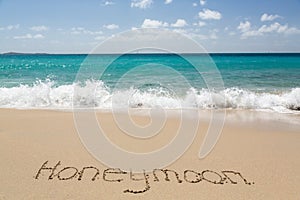 Honeymoon written in sand with sea surf