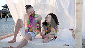 Honeymoon, young people in colorful wreaths sunbathe in bungalow on beach, Backlight, pair of lovers at Hawaii, summer