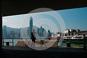 Silhouette of a man on mobile phone looking at   Tsim Sha Tsui Star Ferry Pier  and Hong Kong Island skyline