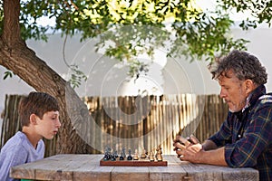 Honing his chess skills with his granddad. a young boy playing chess with his grandfather.