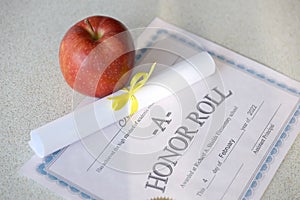 A honor roll lies on table with small scroll and red apple. Education documents