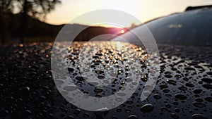 Hood of car with big water droplets after warm heavy summer rain. Blurry droplets at background highlighted by Sunset backlight
