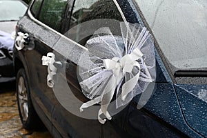 The hood of a dark blue car is decorated with a flowers with white ribbon