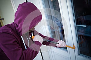 Hooded burglar forcing window to rob in the house