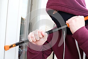 Hooded burglar forcing window to rob in the house