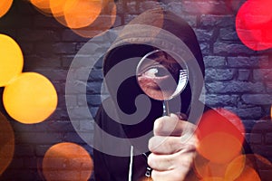 Hooded computer hacker with magnifying glass