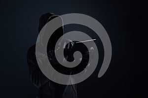 Hooded computer hacker with obscured face using digital tablet