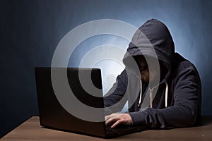 Hooded computer hacker stealing information with laptop