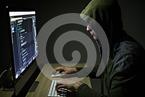 Hooded computer hacker stealing information with pc in Dark room background