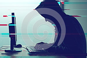 Hooded computer hacker working on desktop PC computer
