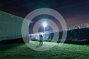 A hooded figure, silhouetted against a street light on an industrial estate at night