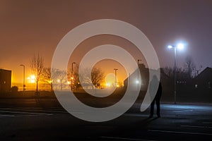 A hooded figure standing in an empty industrial estate on a misty winters night photo
