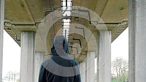 A hooded figure standing underneath a motorway bridge