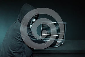 Hooded hacker with anonymous mask using laptop to steal data