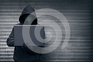 Hooded hacker with mask holding laptop while typing