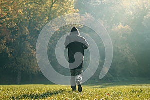 Hooded man jogging in the park in early autumn morning