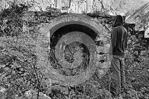 Hooded man next to arched recess of rural ruin photo