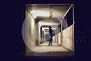 Hooded man standing in construction passage at night.