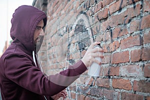 Hooded tagger writing graffiti on urban walls