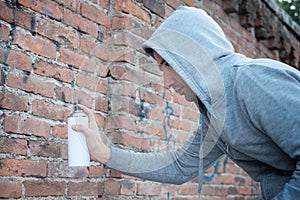 Hooded tagger writing graffiti on urban walls