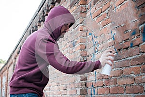 Hooded tagger writing graffiti on urban walls