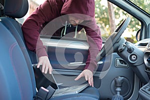 Hooded thief stealing a computer laptop from a parked car
