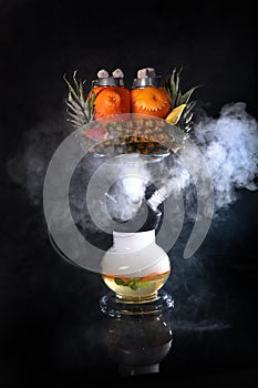 Hookah on pineapples and oranges. Smoking device. Hookah on a black background with a mixture of citrus and pineapple