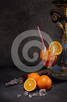 Hookah shisha, glass of cocktail, oranges and ice on dark gray background with copy space. Cocktail Aperol spritz. Hookah bar