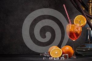 Hookah shisha, glass of cocktail, oranges and ice on dark gray background with copy space. Cocktail Aperol spritz. Hookah bar