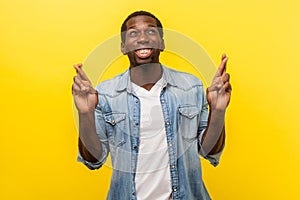 Hope for good luck. Portrait of young man crossing his fingers and looking up. indoor studio shot isolated on yellow