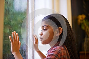 Hope it stops raining so I can go outside and play. Shot of a cute little girl looking out the window on a rainy day.