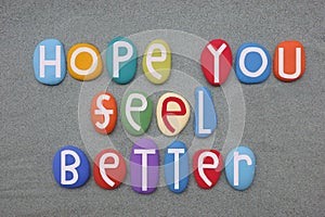 Hope you feel better, friendly message composed with multi colored stone letters over green sand