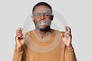 Hopeful black man in glasses cross fingers making wish