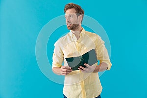 Hopeful casual man looking away while holding a book