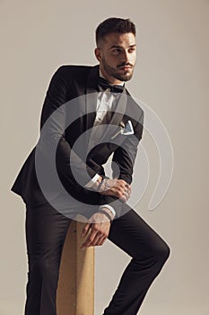 Hopeful groom leaning on leg and looking away, wearing tuxedo