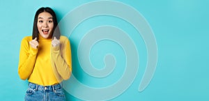 Hopeful and happy asian woman looking with amazement and hope at camera, winning, standing over blue background