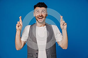 Hopeful man looking up and holding fingers crossed isolated over blue background