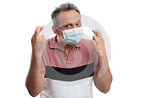 Hopeful man wearing medical mask and showing fingers crossed as good luck concept