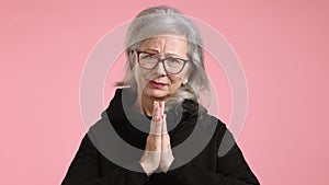 Hopeful mature woman imploring with hands clasped on pink