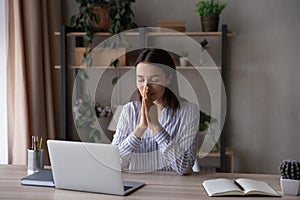 Hopeful religious businesswoman joining hands in prayer, sitting at desk