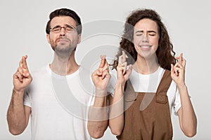 Hopeful young couple cross fingers making wish together