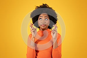 Hopeful young woman with afro hair crosses her fingers for good luck