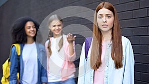 Hopeless bullying victim looking camera, female classmates discussing behind